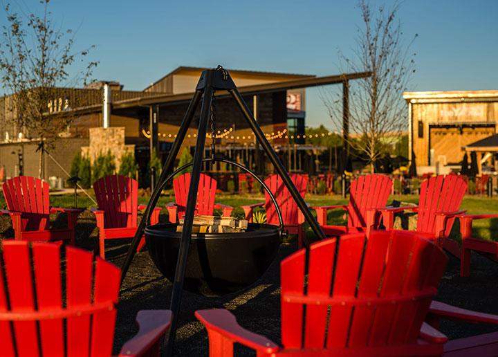 Red adirondack chairs arranged in a circle around a fire pit cauldron outside of 2 Silos in Manassas, VA